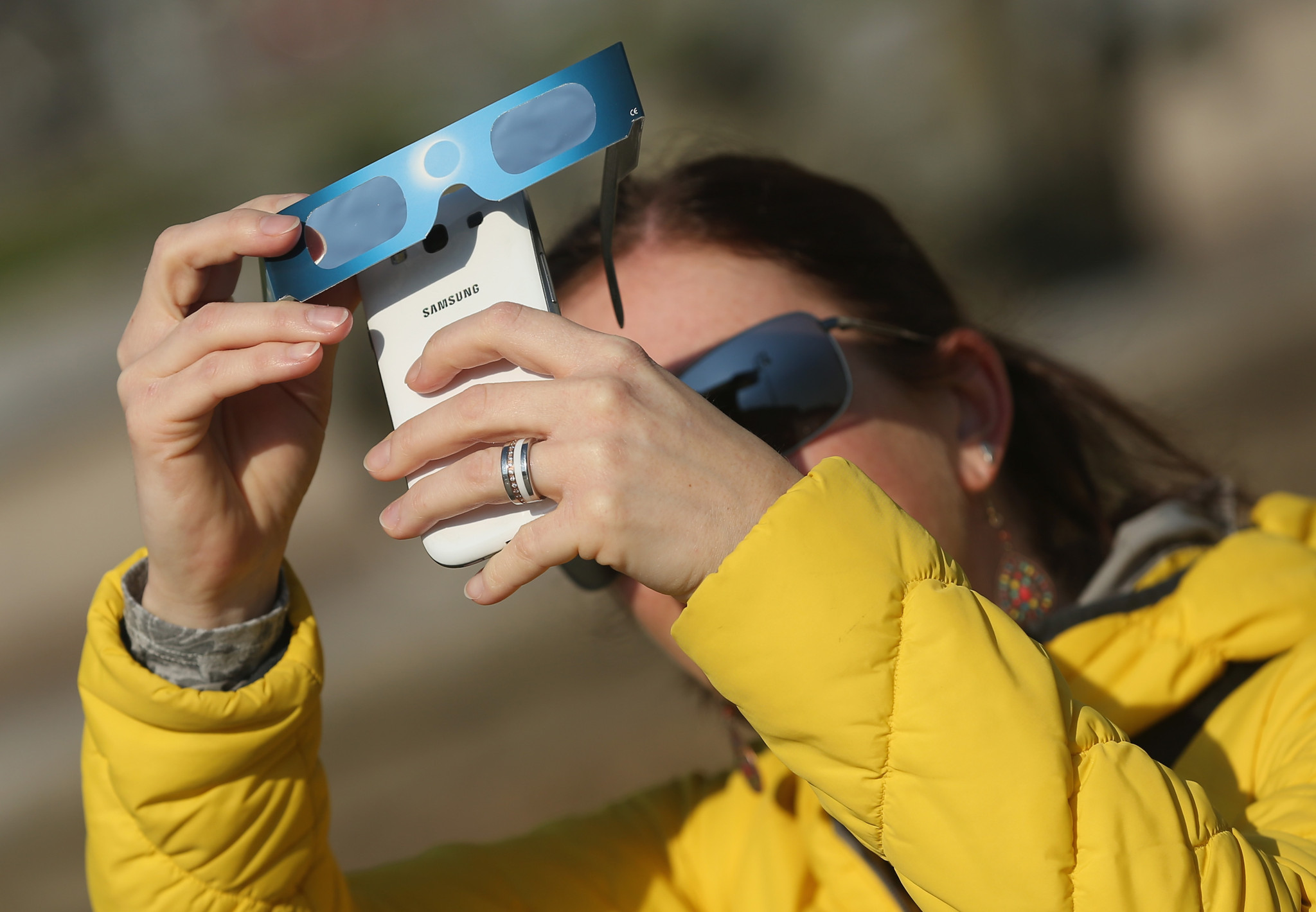 Frau mit Sonnenfinsternisbrille und Samsung-Smartphone fotografiert die partielle Sonnenfinsternis am 20. März 2015 nahe dem Brandenburger Tor in Berlin.