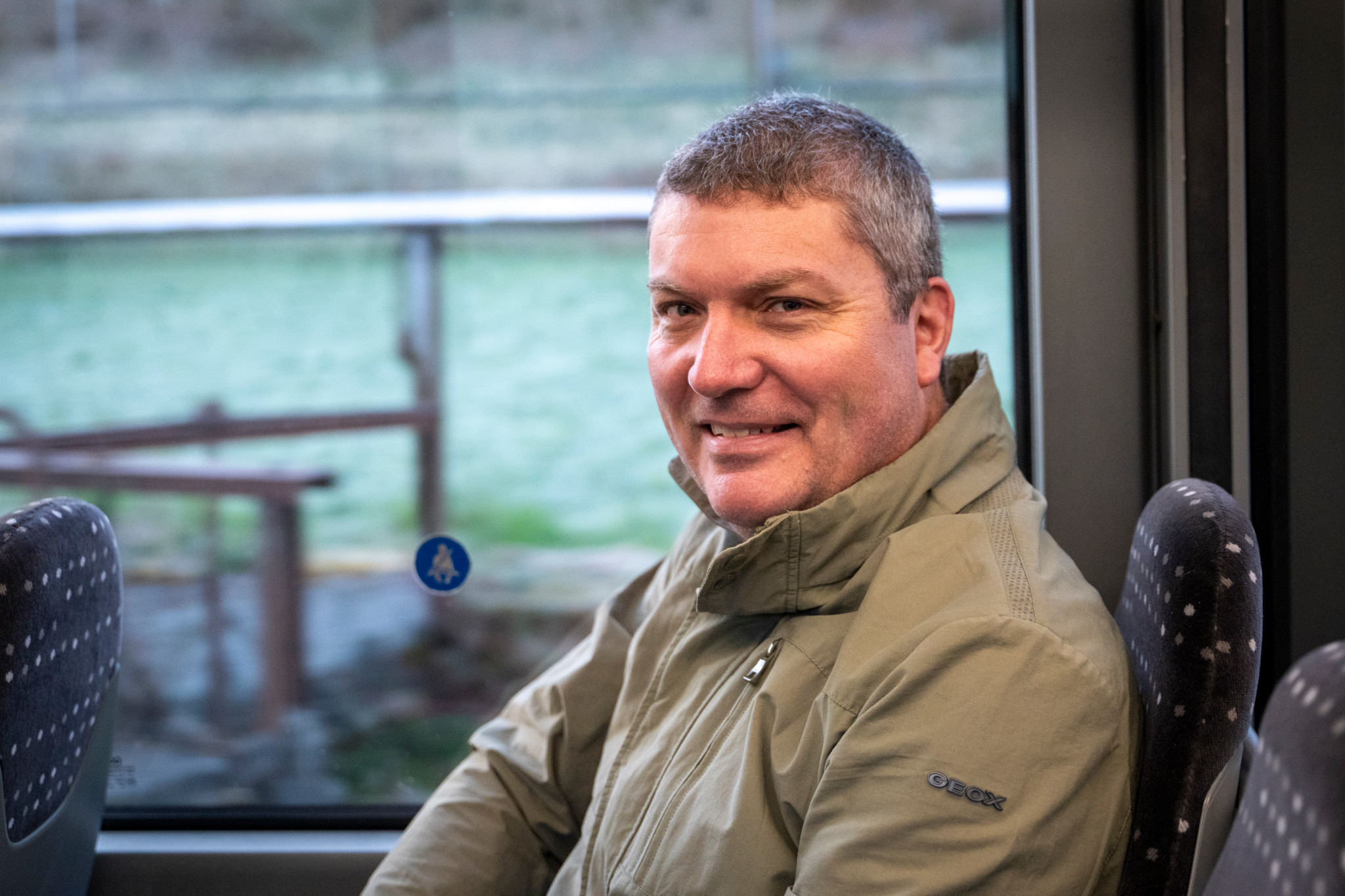 Godi Studer sitzt in einem Bus. Hintergrund zeigt eine Landschaft durch das Fenster. Foto von Marcel Bieri, 8. April 2025.