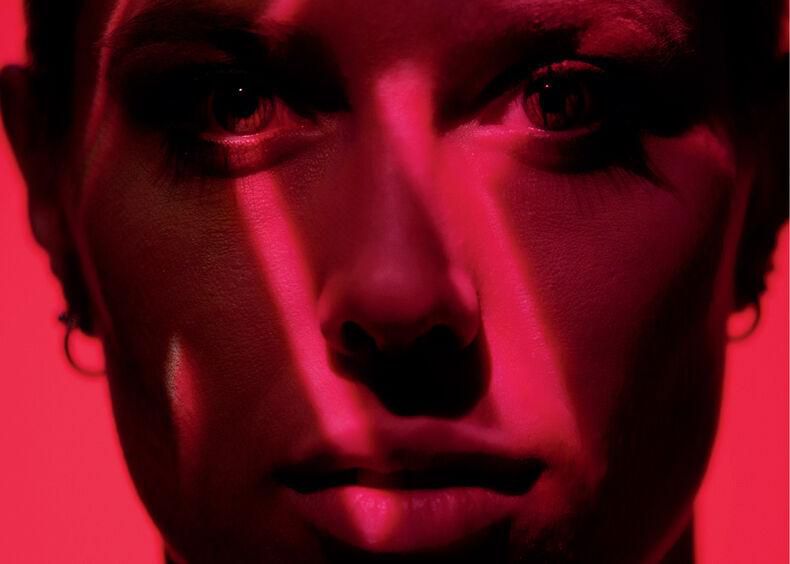 Visage éclairé par des lumières rouges et roses avec des ombres diagonales.