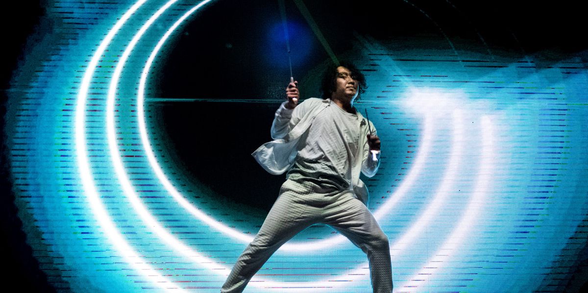 Une personne en tenue blanche effectue des mouvements lumineux artistiques dans un spectacle avec des effets lumineux circulaires.