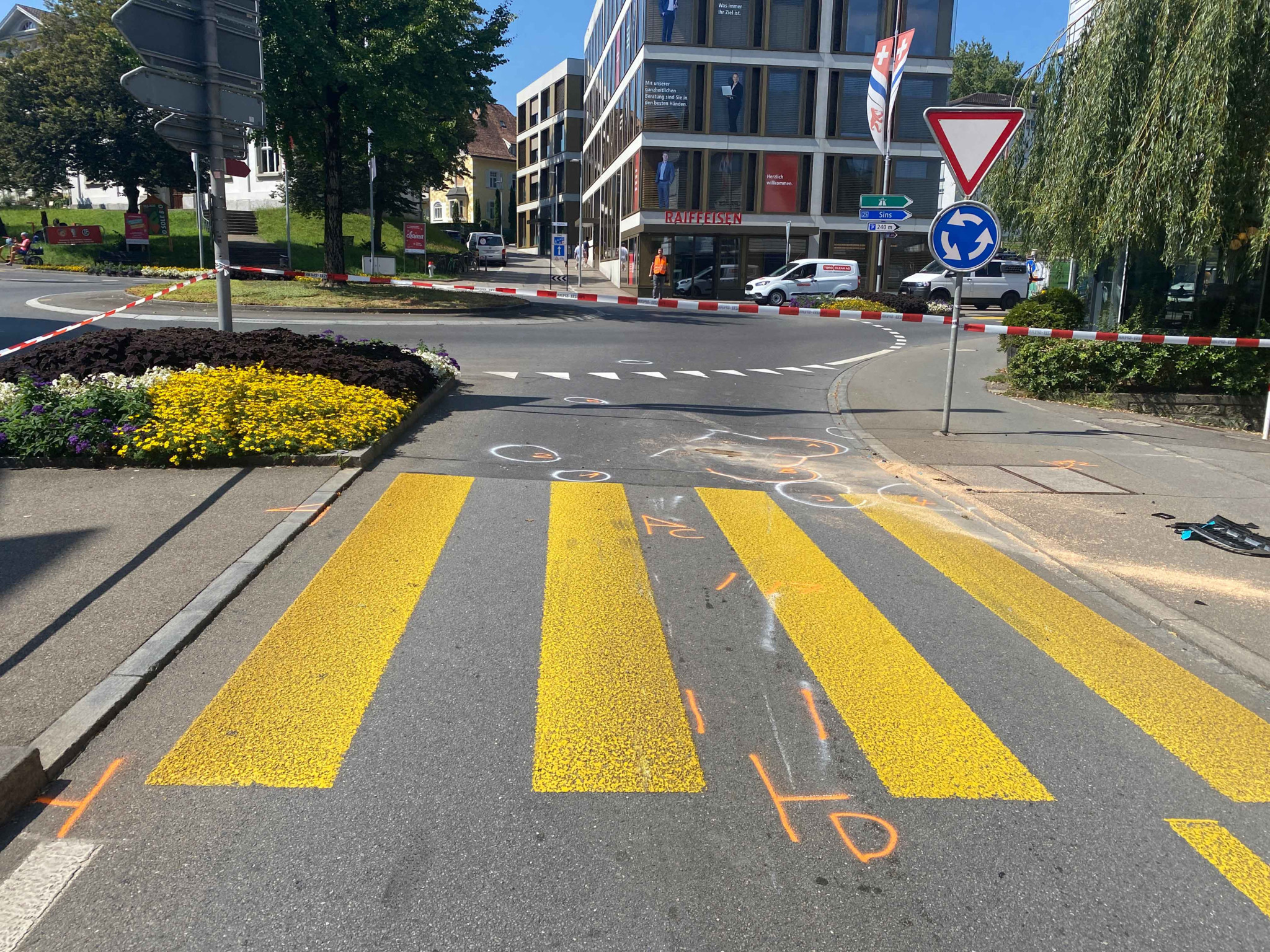 Zebrastreifen vor einem Kreisverkehr mit Absperrband und Strassenmarkierungen in einer städtischen Umgebung.