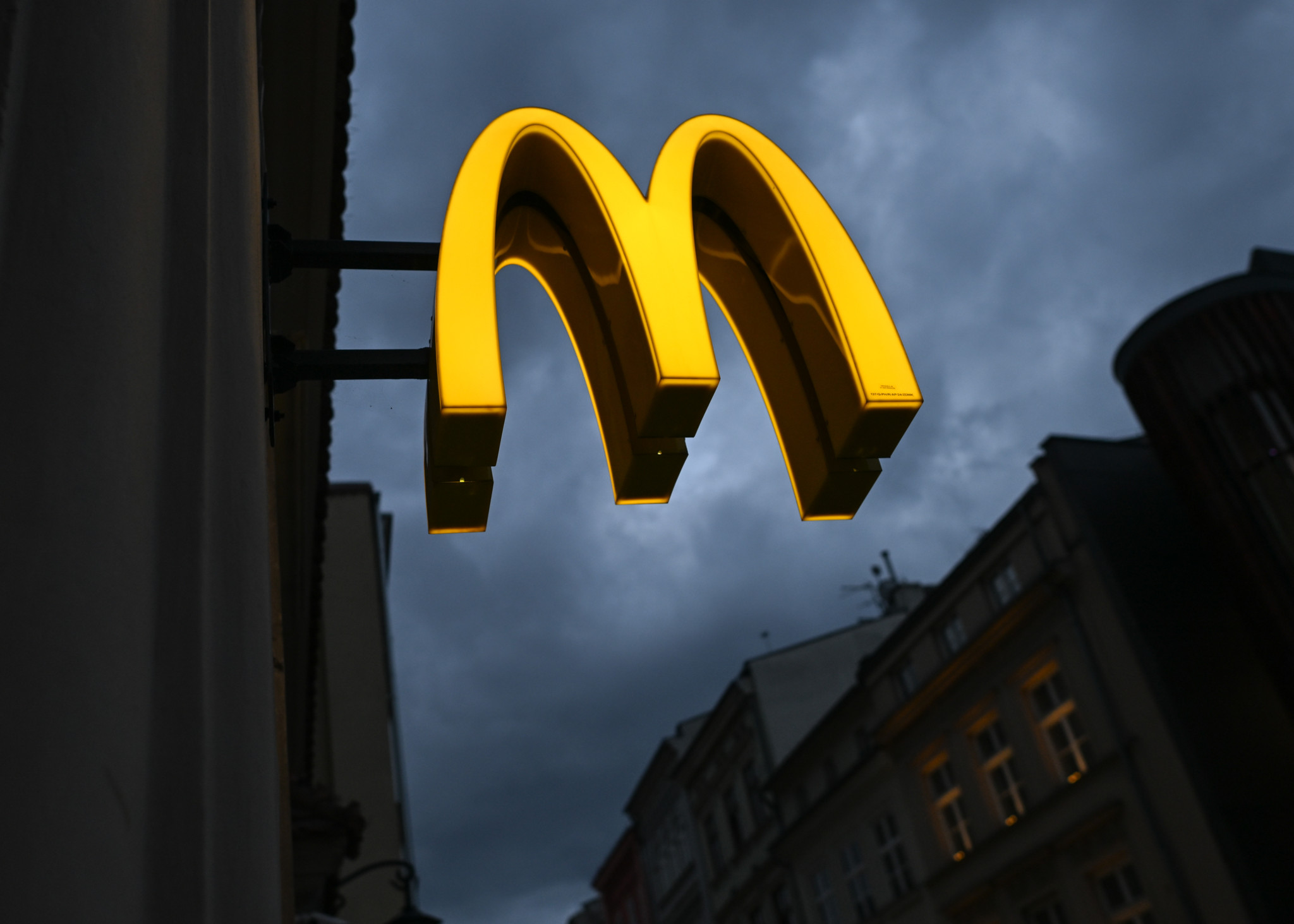 Beleuchtetes McDonald’s-Logo vor dramatischem, stürmischem Himmel an Fassade eines historischen Gebäudes in Krakau, Polen.