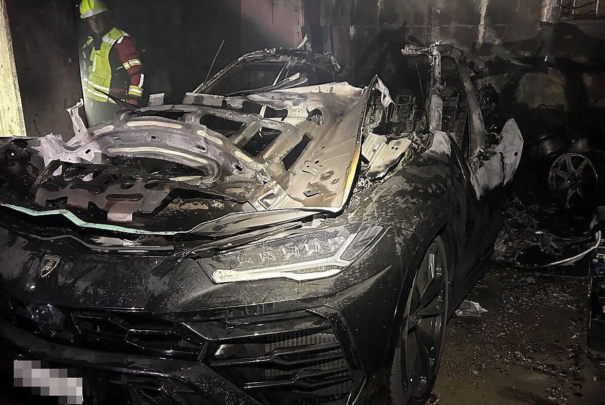 Voiture de luxe endommagée par un incendie dans un garage, avec un pompier examinant la scène.