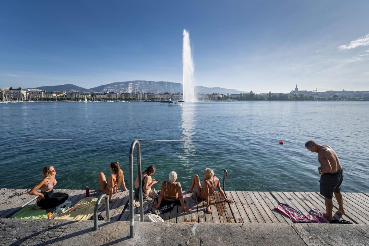 This photograph taken on October 5, 2023, shows lake-goers sitting and laying next to Geneva Lake at the 'Bains des Paquis' public bath downtown Geneva, with the Geneva's landmark fountain, known as "Jet d'Eau" in the background, as unusual warm temperature for the season hit Switzerland. (Photo by Fabrice COFFRINI / AFP)