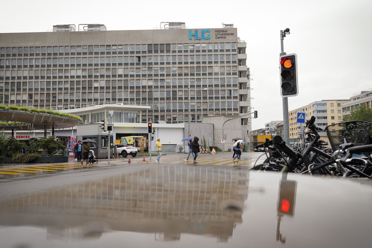 Vue extérieure d’un bâtiment des Hôpitaux Universitaires de Genève avec un feu de signalisation rouge et quelques cyclistes.