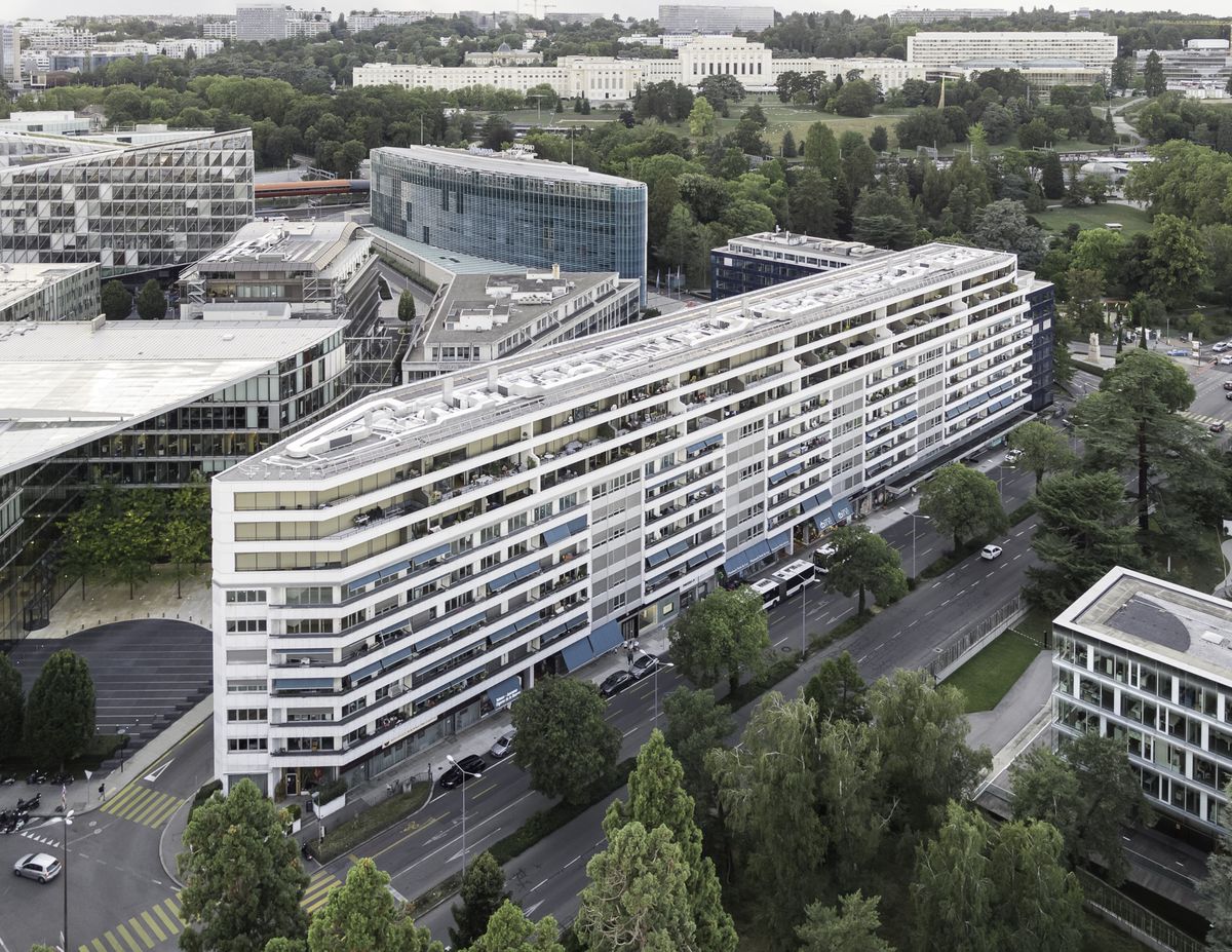 Vue aérienne d'un complexe de bâtiments modernes dans une zone urbaine, entouré de verdure et de routes.