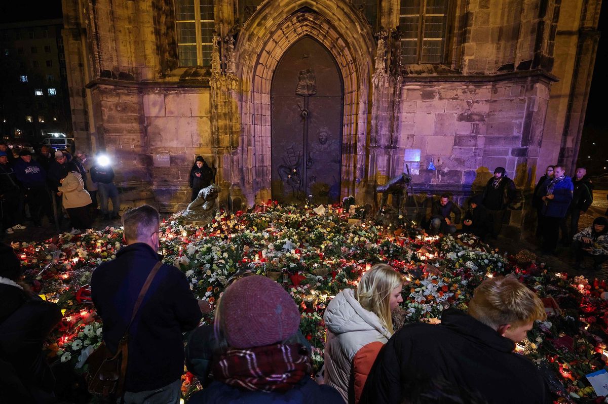 Menschen stehen an einem provisorischen Denkmal in Magdeburg nahe dem Ort eines Autoangriffs auf einen Weihnachtsmarkt, umgeben von Kerzen und Blumen, am 21. Dezember 2024.