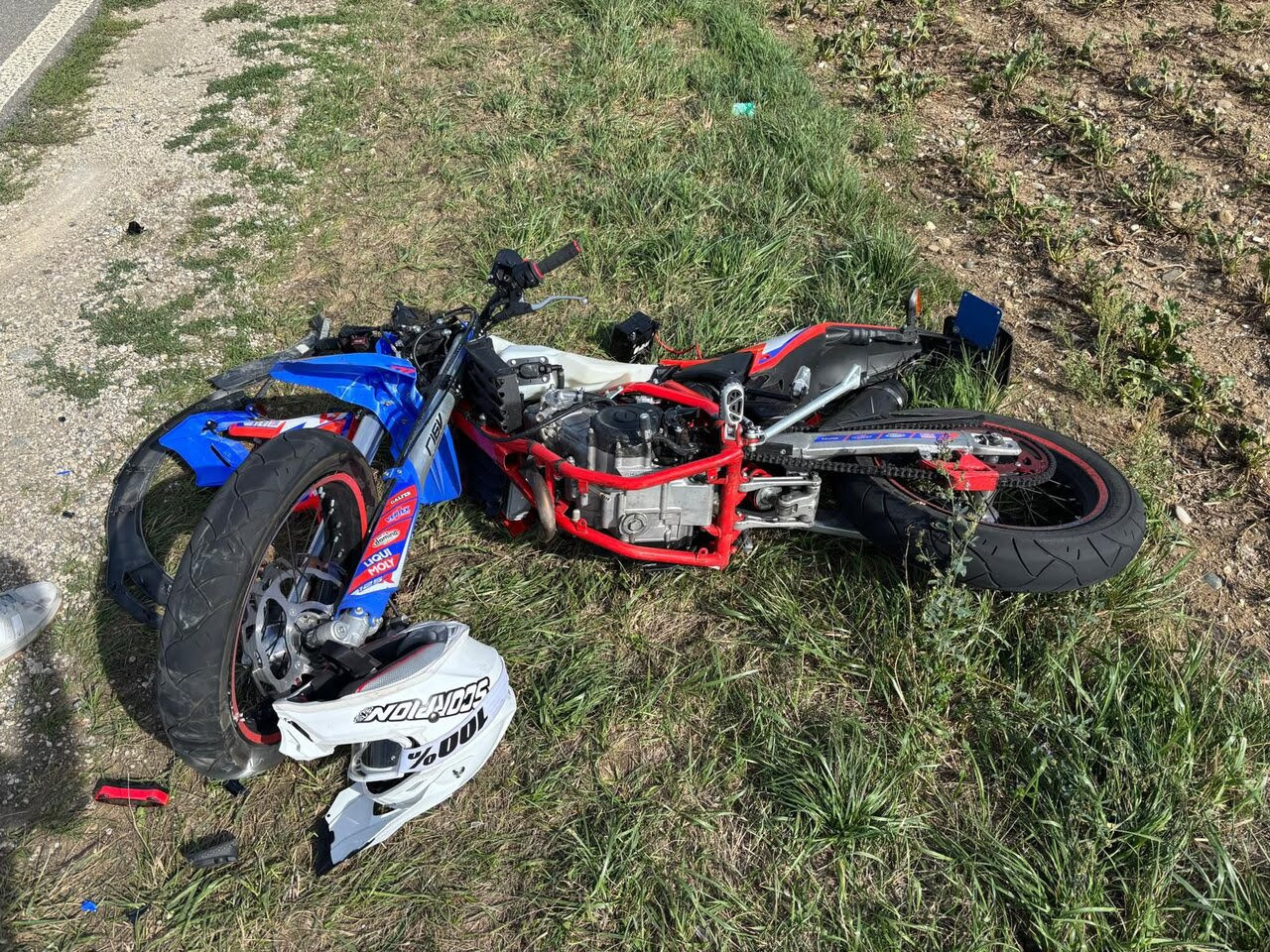 Verunfalltes blau-rotes Motorrad liegt nach einem Unfall im Gras am Strassenrand, Verkleidungsteile abgebrochen.