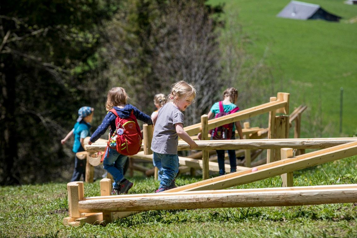 Die Kinder spielen an den fix installierten Holzmurmelbahnen am Kugelweg im Hasliberg.