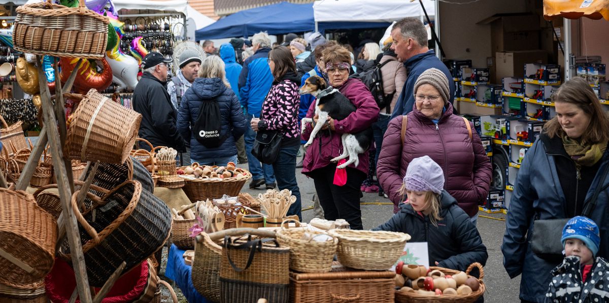 Besucher auf dem Jahrmarkt in Schwarzenegg stöbern an verschiedenen Ständen voller Körbe und Spielzeug.