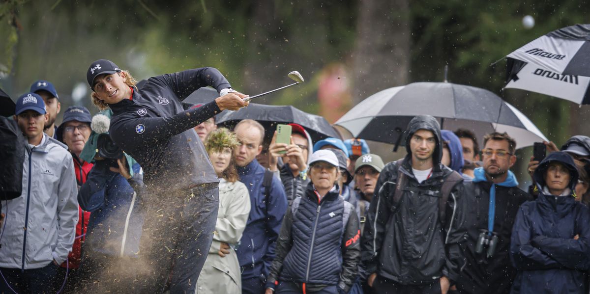 Cedric Gugler frappe un coup lors de la quatrième et dernière manche du DP World Tour Omega European Masters à Crans-Montana, Suisse, entouré de spectateurs sous des parapluies.