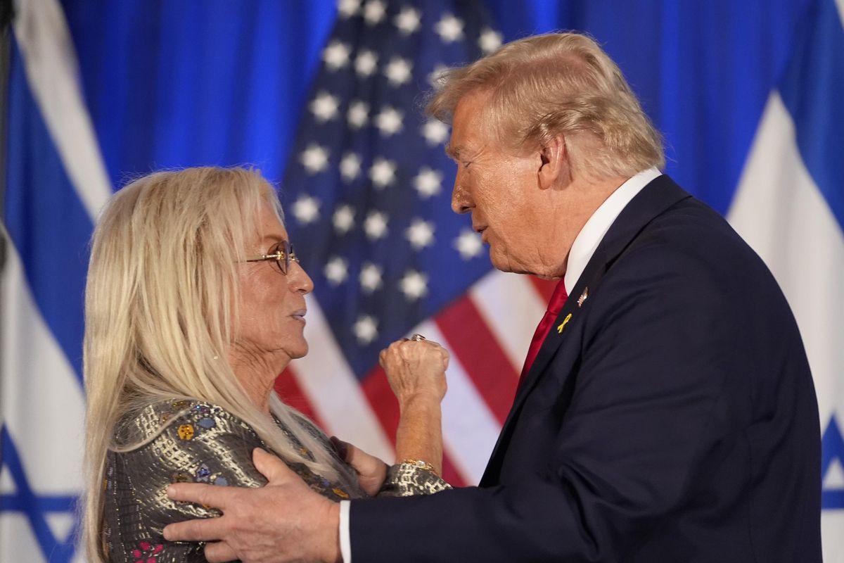 Donald Trump enlaçant Miriam Adelson lors d'un événement à Miami marquant un an depuis l'attaque du 7 octobre sur Israël, avec des drapeaux en arrière-plan.