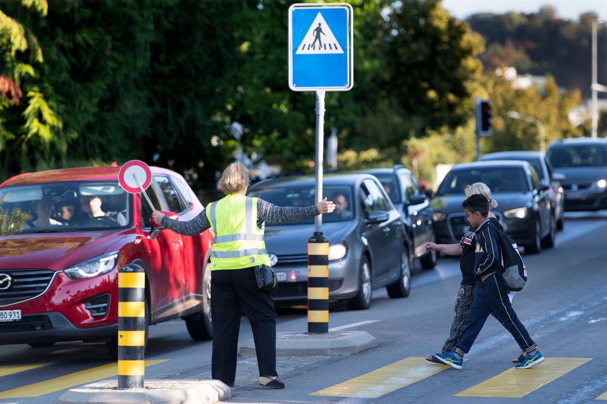 Un patrouilleur scolaire aide a faire traverser sur un passage pieton lors de la campagne de prevention routiere pour la rentree scolaire 2018 ce lundi 27 aout 2018 a Lausanne. A l'occasion de la rentree scolaire, la Police de Lausanne menera une campagne de prevention accompagnee de differents controles. Ces actions, se deroulant aux abords des etablissements scolaires, ont pour but de rappeler aux conducteurs les regles elementaires de securite pour leurs propres enfants mais aussi pour les autres ecoliers qui se trouvent sur le chemin des classes. (KEYSTONE/Laurent Gillieron)
