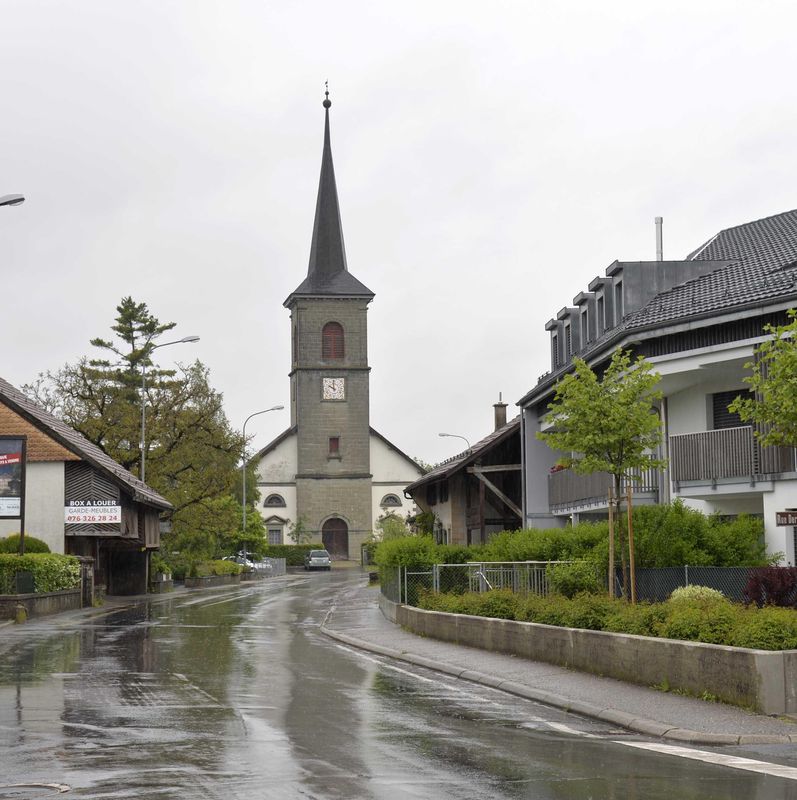 Rue humide à Palézieux Village avec une église au clocher pointu en arrière-plan.