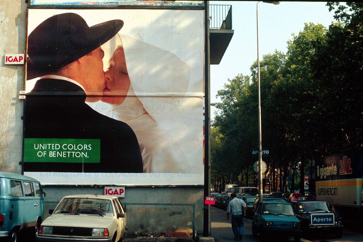 Affiche publicitaire Benetton à Milan par Oliviero Toscani, montrant un couple s’embrassant, avec des voitures et arbres en arrière-plan.