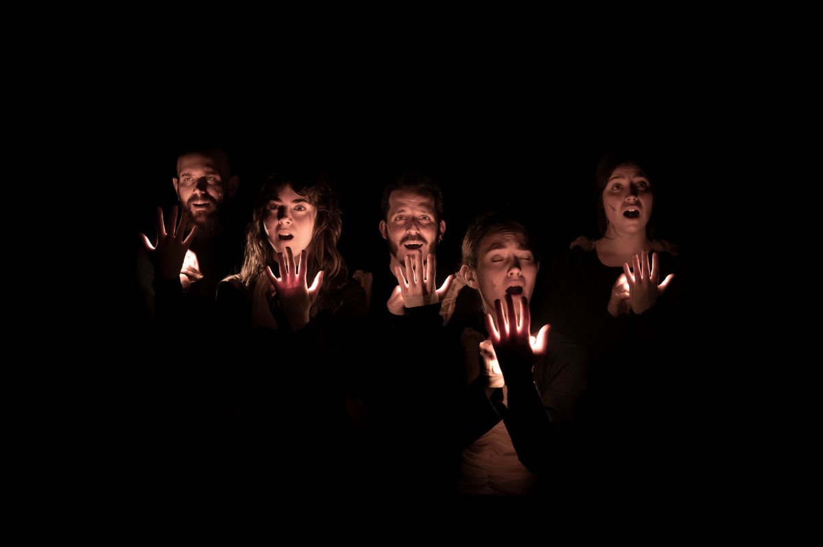 Cinq personnes dans l'obscurité, montrant leurs mains illuminées par une source de lumière interne, produisant un effet dramatique.