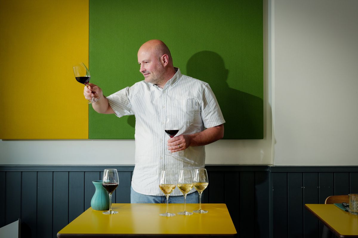 Bertrand Lutaud dans son restaurant Yeast à Carouge, dégustant du vin devant une table avec plusieurs verres. Il célèbre son titre prestigieux en sommellerie.