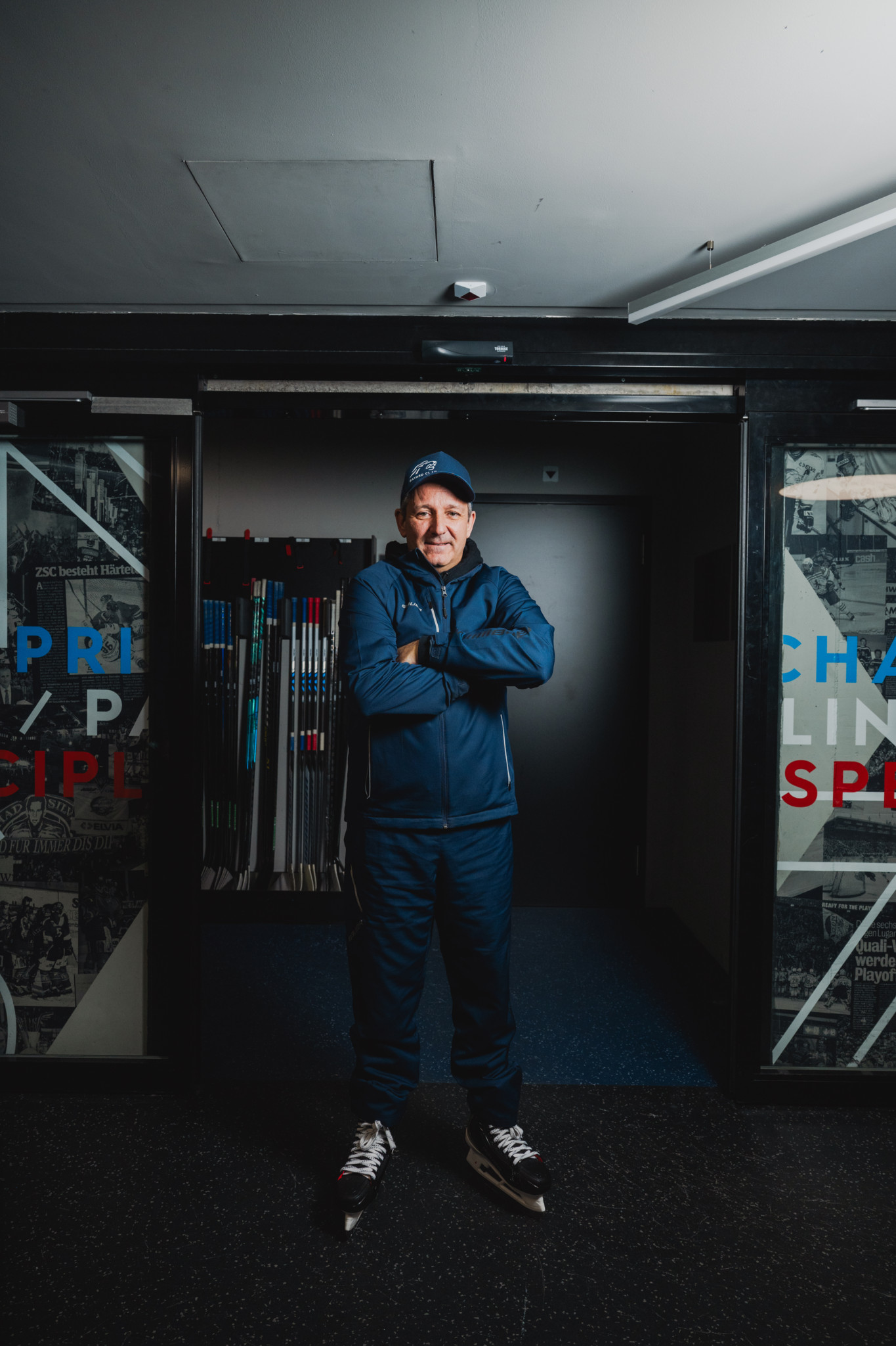 ZSC-Trainer Marco Bayer steht mit verschränkten Armen in der Swiss Life Arena, umgeben von Hockeyschlägern.
