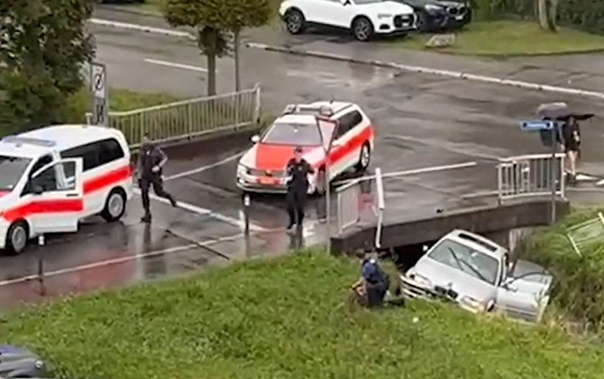 Polizeibeamte reagieren auf eine Situation an einer Strassenecke, wo ein Auto im Graben steckt, während andere Autos und Personen sichtbar sind.
