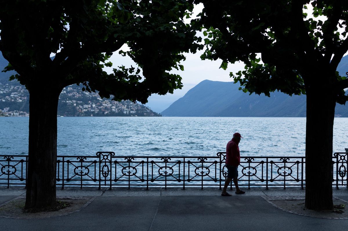 Un vieil homme marche le long de la promenade du lac à Lugano en soirée, avec des montagnes en arrière-plan, photographié le 3 août 2023.