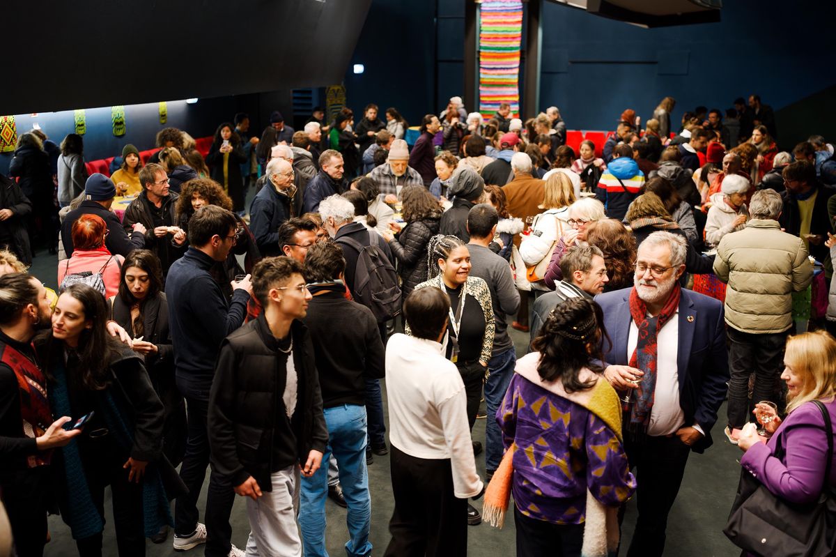 Un groupe important de personnes socialise lors d'un événement dans une salle illuminée.