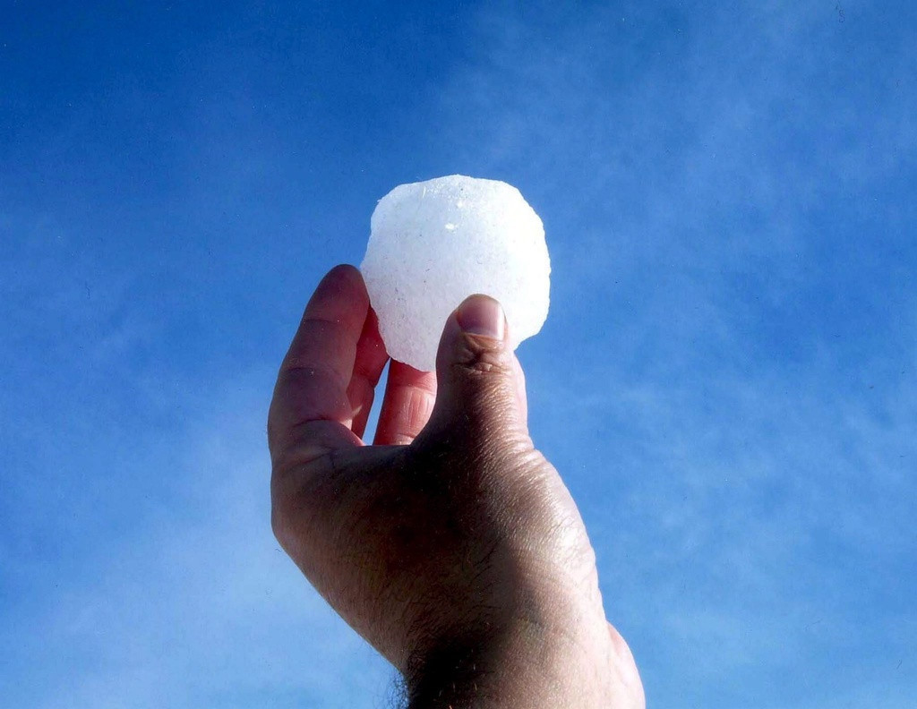 Une main tenant une boule de neige contre un ciel bleu clair.