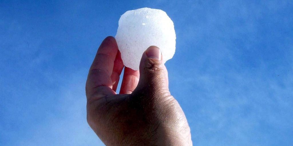 Une main tenant une boule de neige contre un ciel bleu clair.
