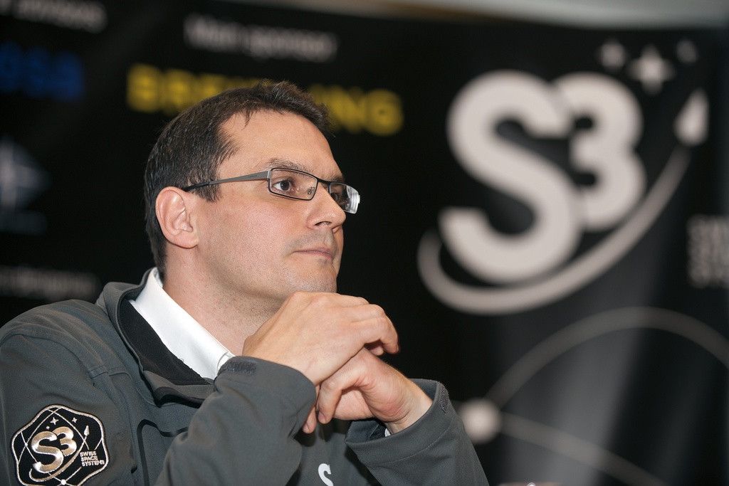 Pascal Jaussi, fondateur et CEO de Swiss Space Systems, lors de l'inauguration dans des locaux provisoires à Payerne, portant des lunettes et un veston avec le logo S3 en arrière-plan.