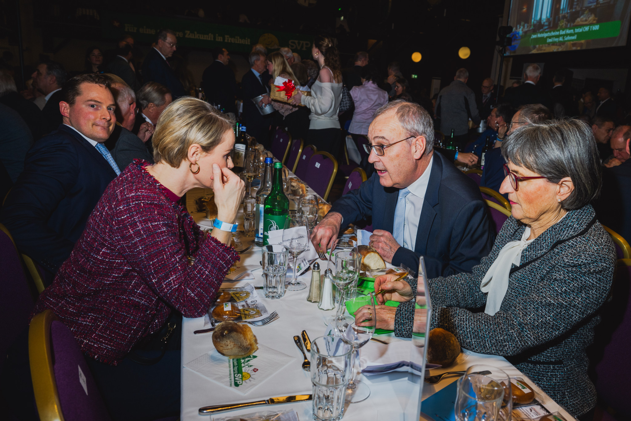 Eine Gruppe von Menschen sitzt an einem Tisch und unterhält sich angeregt auf einer Veranstaltung. Gläser und Flaschen stehen auf dem Tisch.