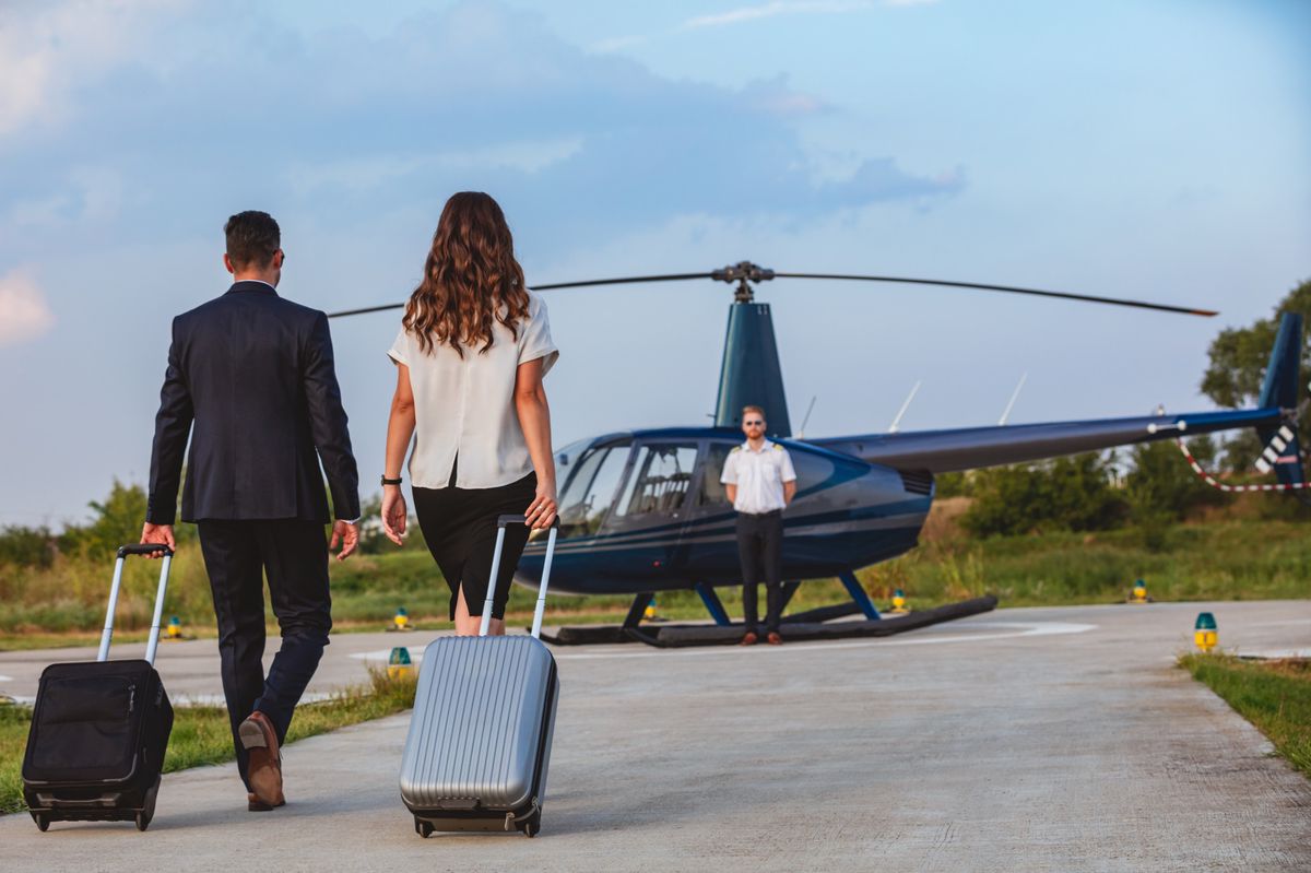 Business couple pulling luggage and walking to helicopter with pilot waiting