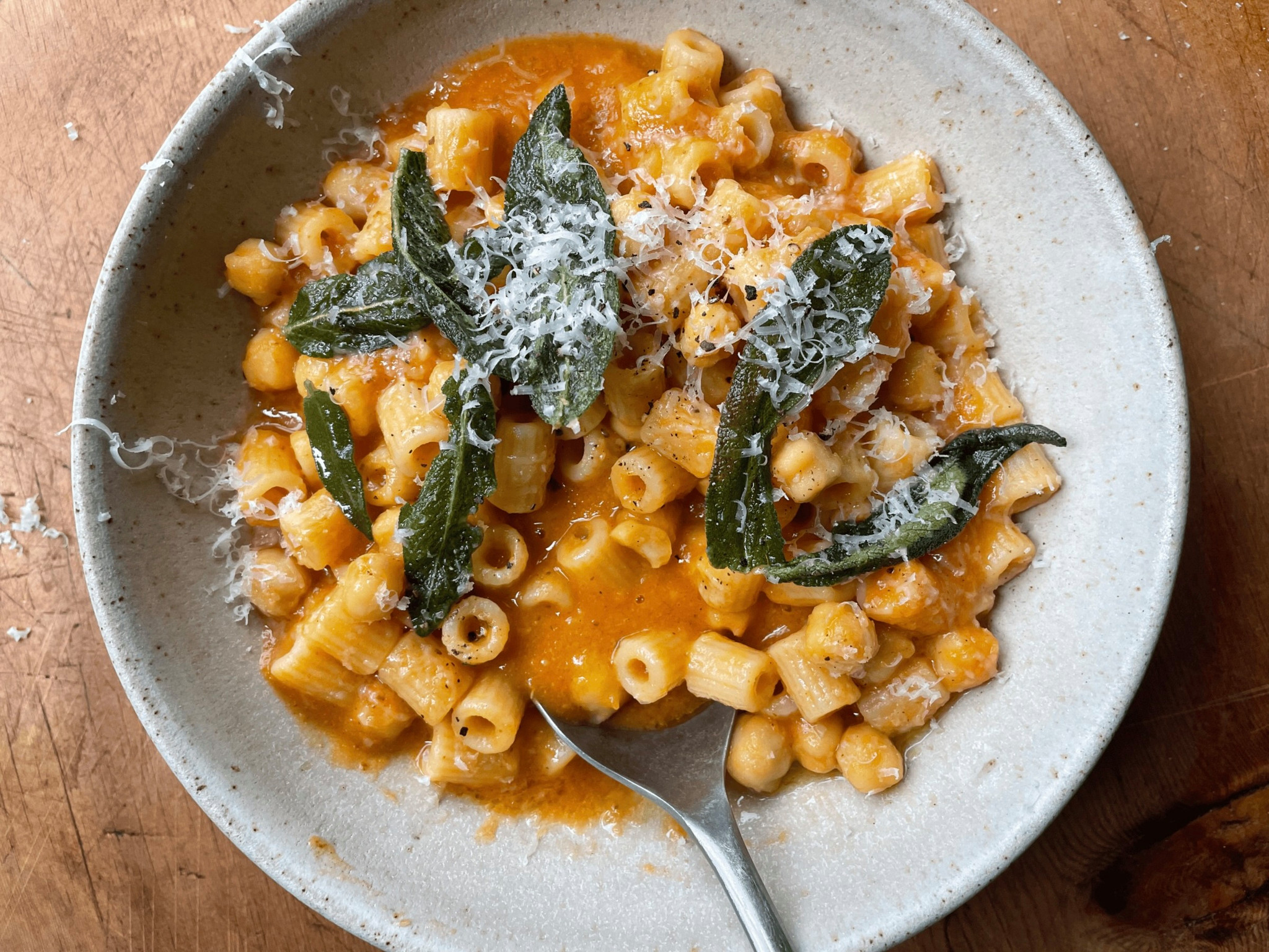 Pasta in cremiger Kürbissauce mit gebratenen Salbeiblättern und geriebenem Parmesan in einem rustikalen Keramikteller.
