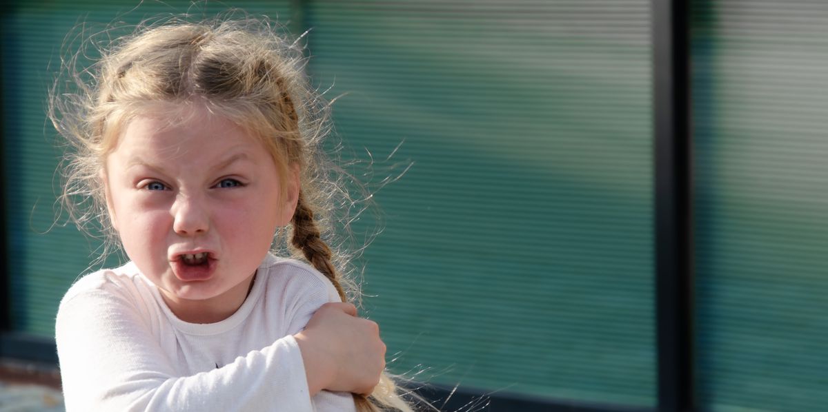 Une petite fille de quatre ans, blonde avec des couettes, exprimant une colère et une agressivité prononcées. Espace pour le texte.