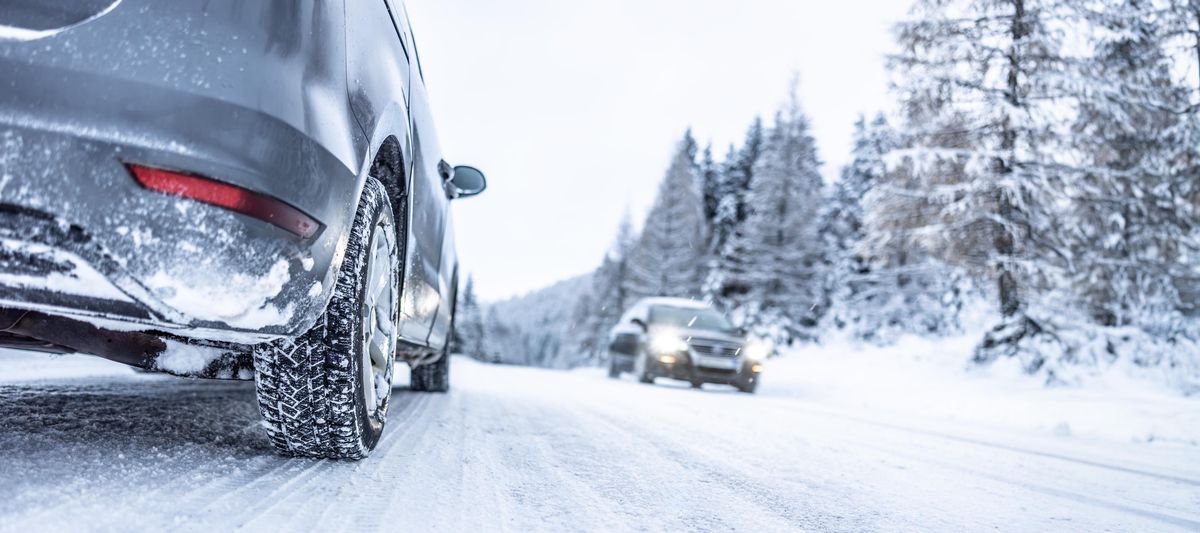 Voitures circulant sur une route enneigée bordée de forêts, sous un ciel d'hiver.
