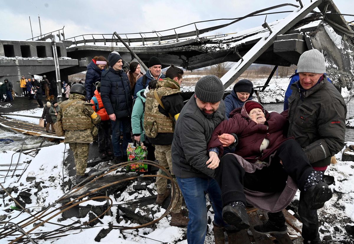Ukrainian soldiers help an elderly woman to cross a destroyed bridge as she evacuates the city of Irpin, northwest of Kyiv, on March 8, 2022. - More than two million people have fled Ukraine since Russia launched its full-scale invasion less than two weeks ago, the United Nations said on March 8, 2022. (Photo by Sergei SUPINSKY / AFP)