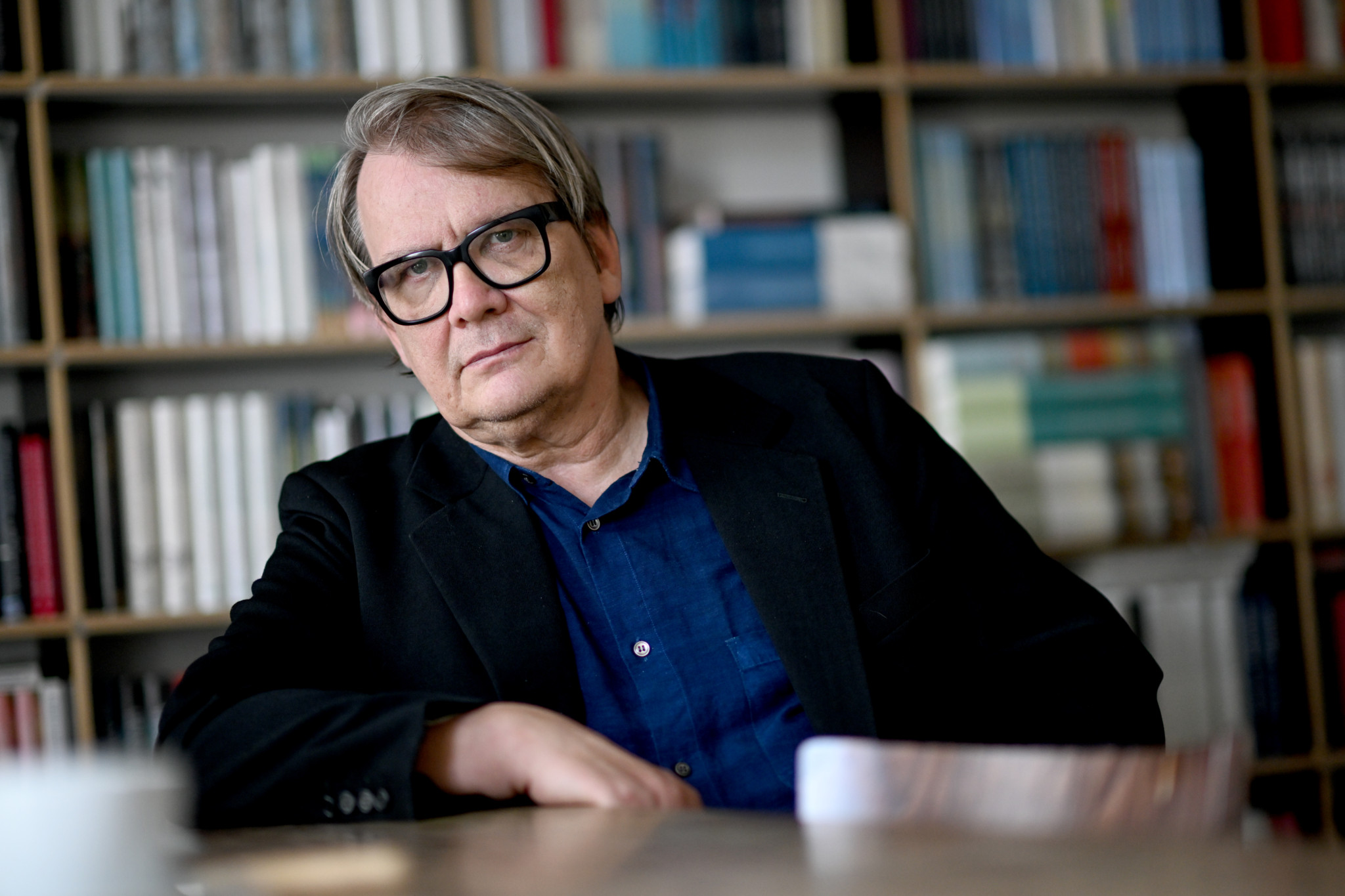 Schriftsteller Sven Regener sitzt vor einem Bücherregal, trägt schwarze Brille und Sakko.