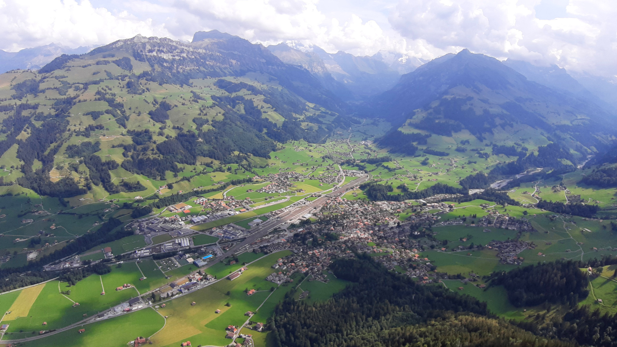 Luftaufnahme von Frutigen in der Schweiz, umgeben von grünen Hügeln und Bergen mit einem klaren Himmel.