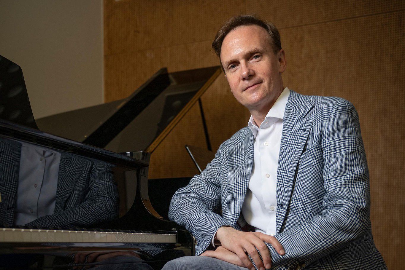 Edgar Philippin, nouveau président de l’OCL, assis à côté d’un piano à l’HEMU, vêtu d’une veste à carreaux.