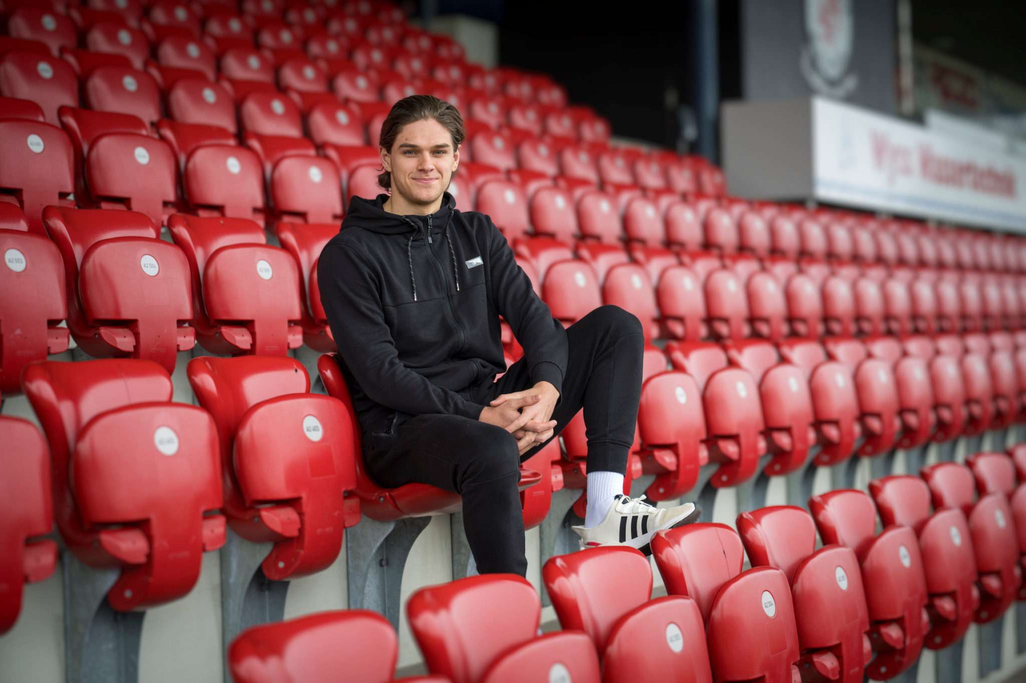Loïc Lüthi vom FC Winterthur sitzt in schwarzem Hoodie entspannt auf roten Stadionrängen.