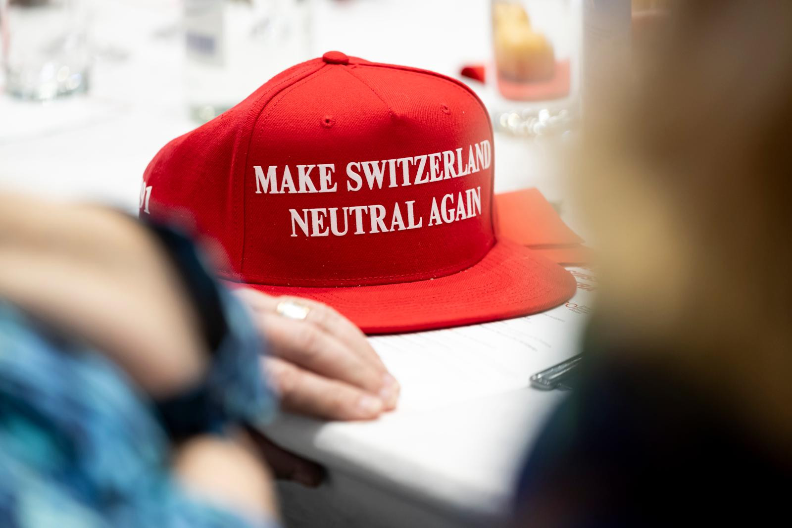 Rote Snapback-Mütze mit der Aufschrift «Make Switzerland Neutral Again» liegt auf einem Tisch.