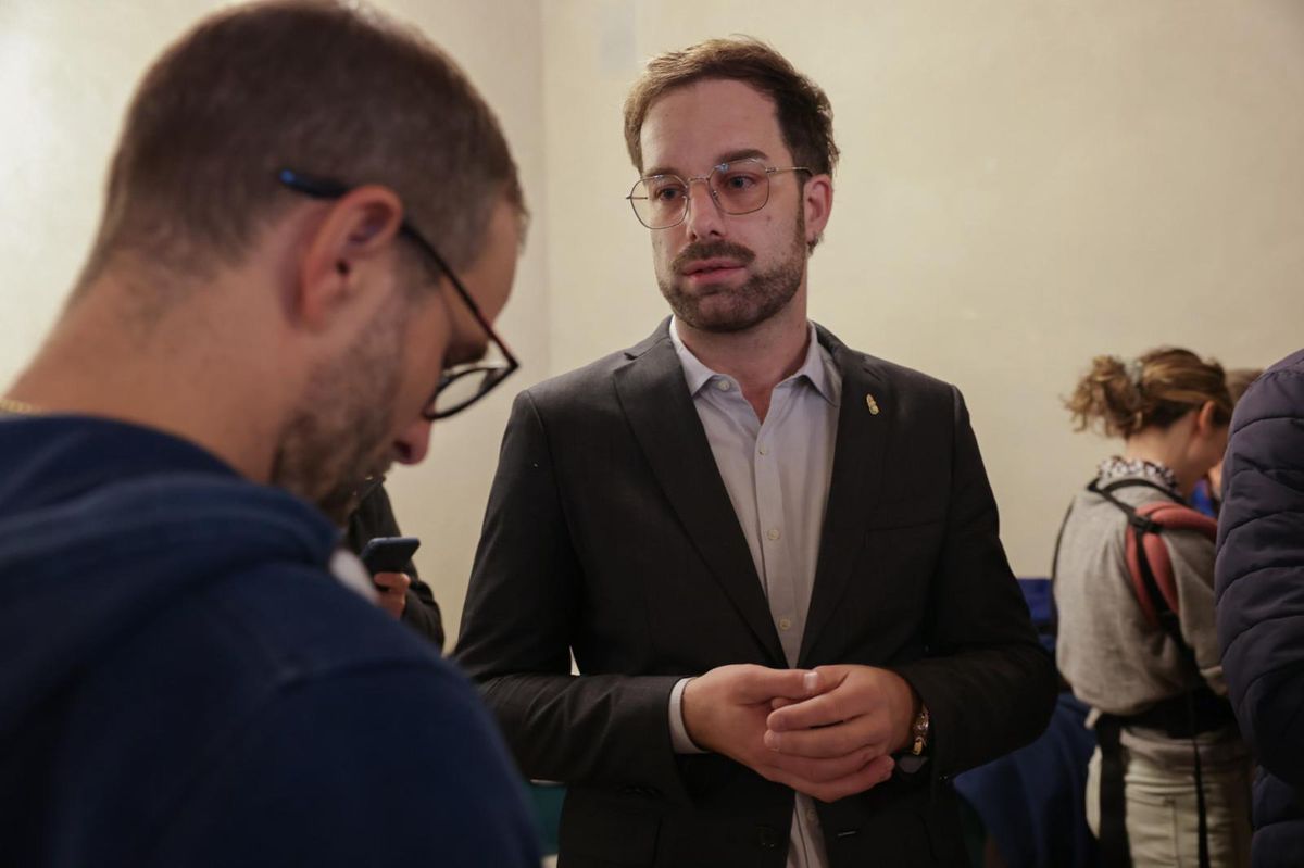 Homme en costume discutant avec un autre homme portant des lunettes dans une pièce éclairée.