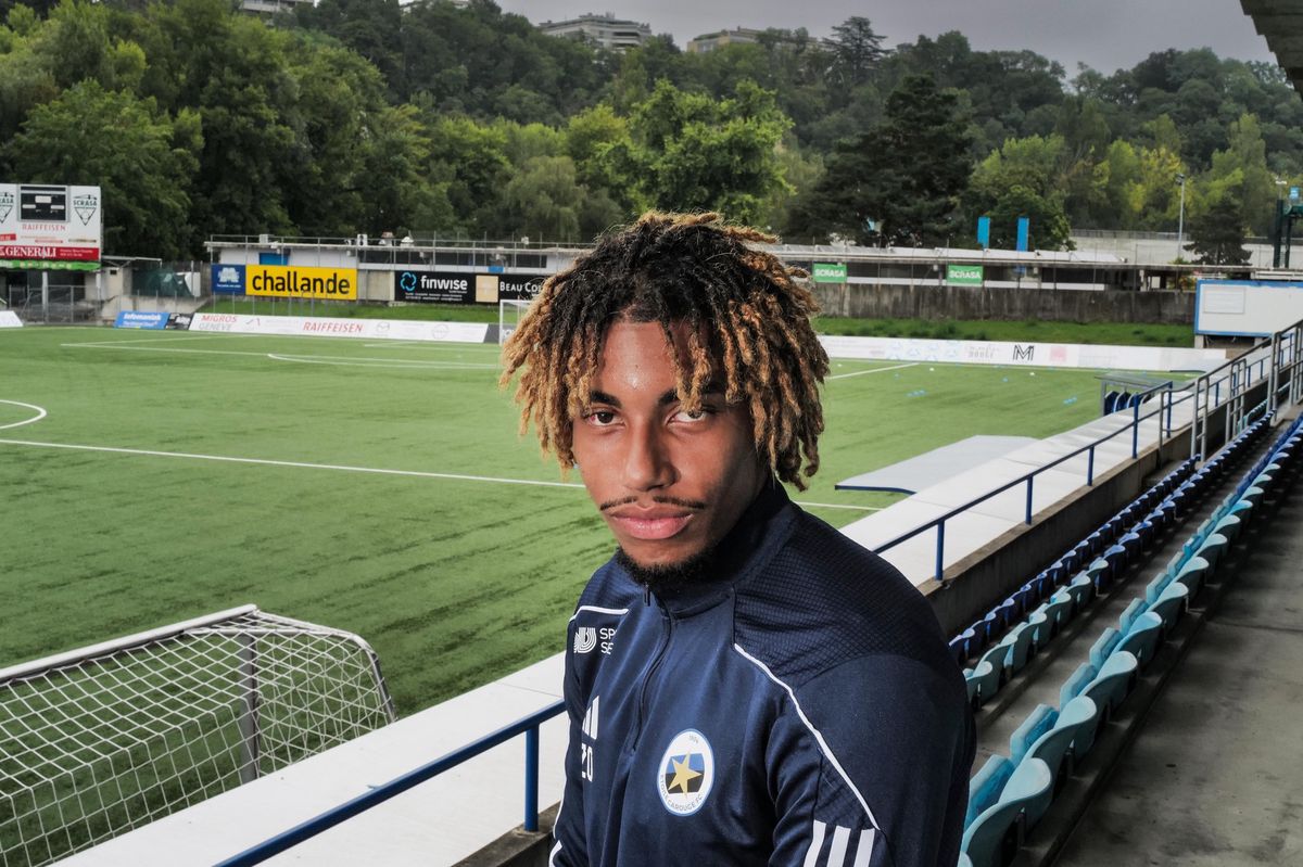 Vincent Nvendo, attaquant d’Etoile Carouge, debout devant un terrain de football vide à Genève.