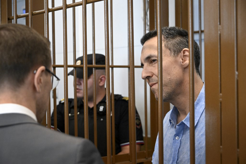 Laurent Vinatier, chercheur français, écoute ses avocats depuis une cage de prévenus pendant une audience au tribunal de district de Zamoskvoretsky à Moscou, le 3 septembre 2024. Un garde de sécurité se tient à l'arrière-plan. (Photo par Alexander NEMENOV / AFP)