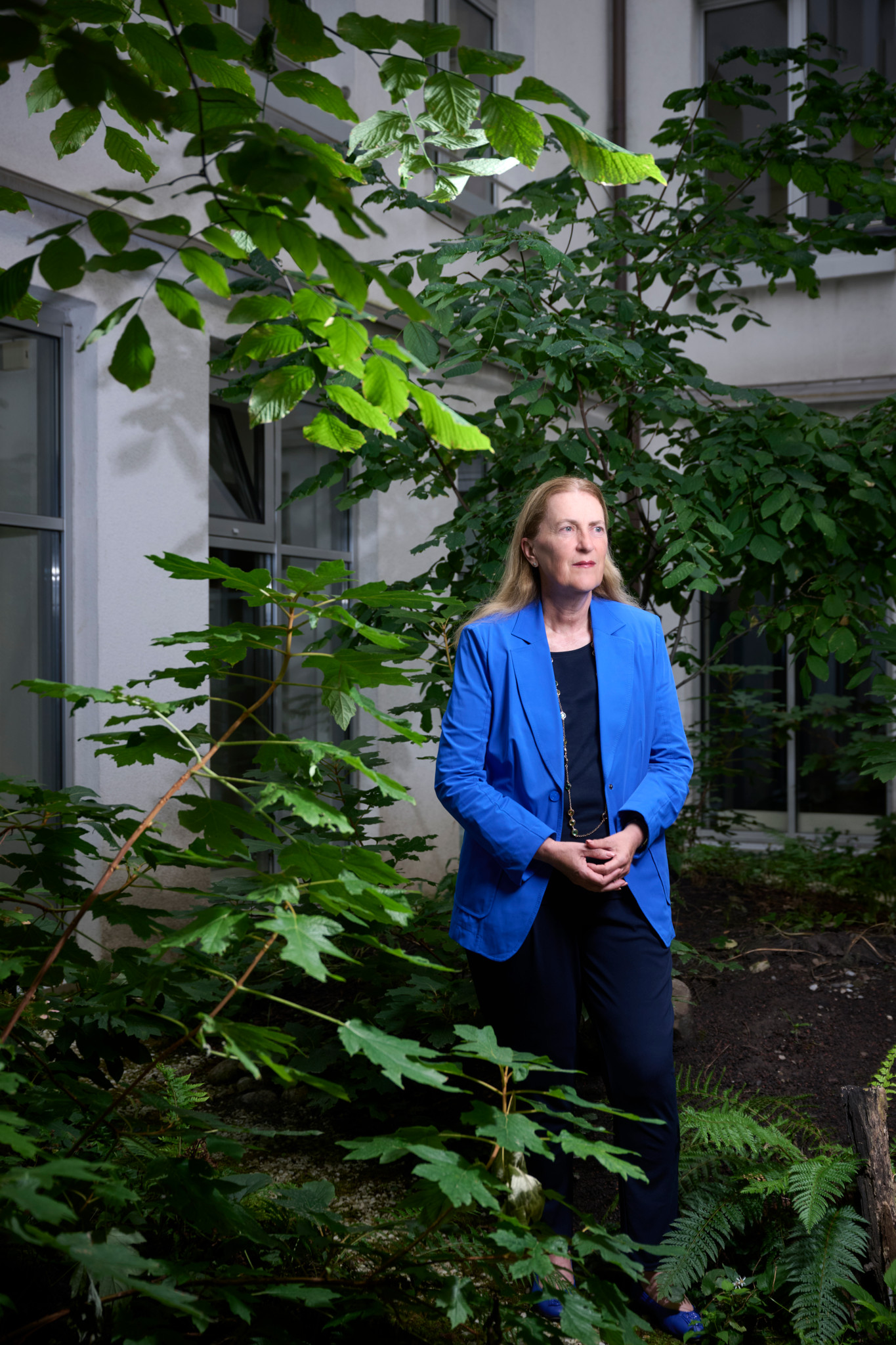 Staatssekretärin Helene Budliger in blauem Blazer, umgeben von Grünpflanzen vor einem Gebäude.