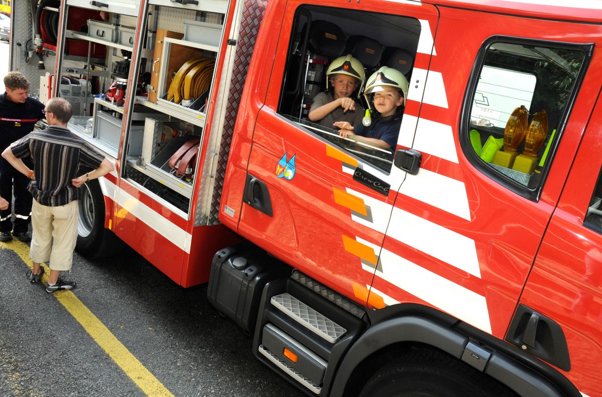 Deux garçons, casque sur la tête, visitent un camion de pompier.