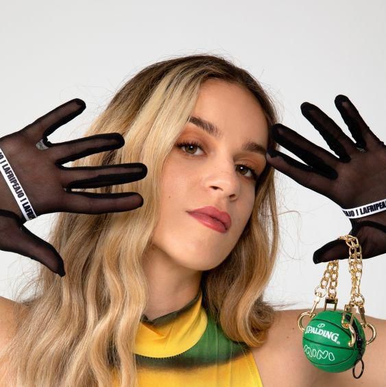 Joana Bender posant avec des gants noirs transparents et un accessoire en forme de montre verte.
