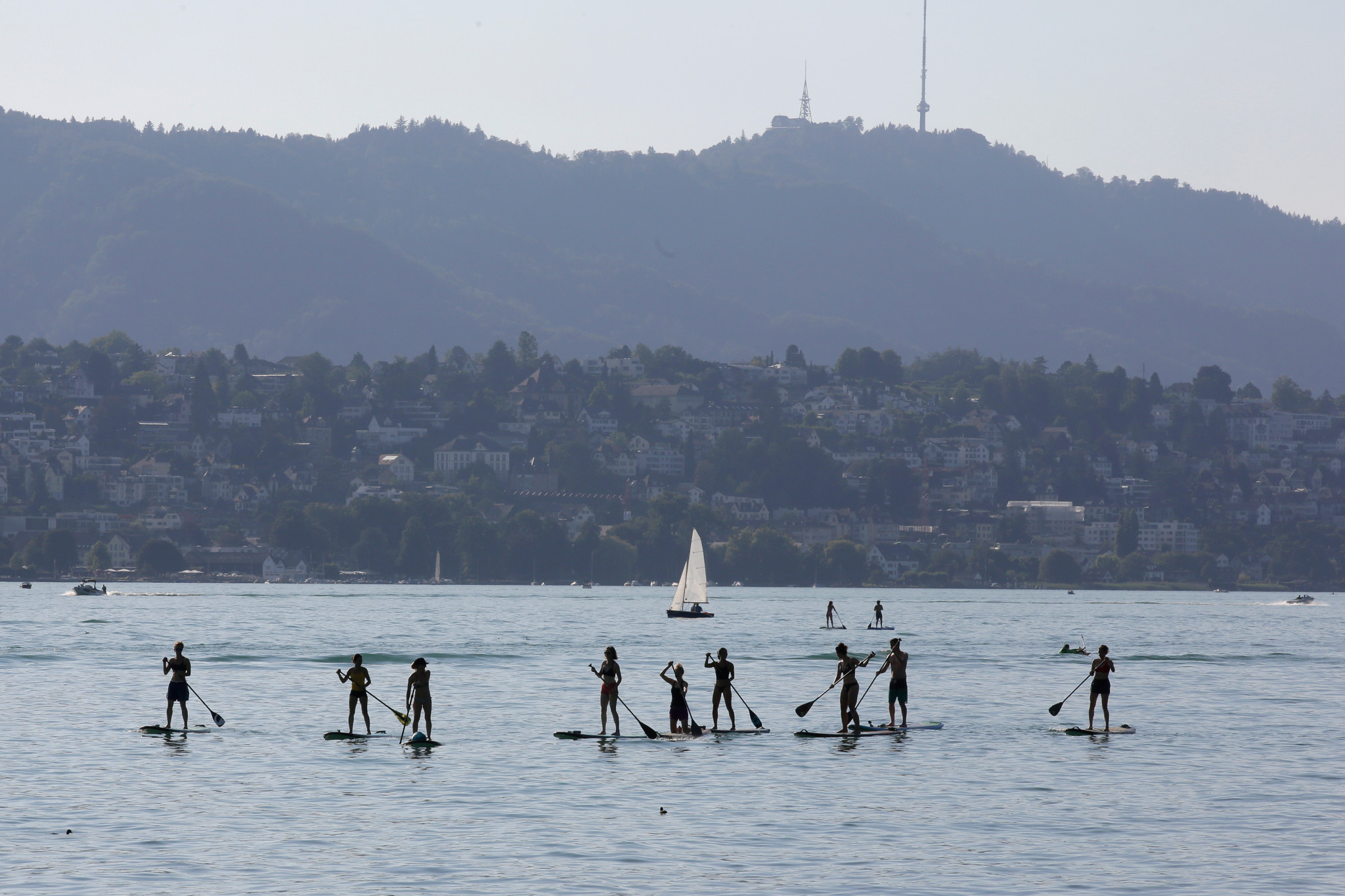 Gruppe macht Yoga auf Stand-up-Paddle-Boards vor Erlenbach am Zürichsee, mit Uetliberg im Hintergrund.