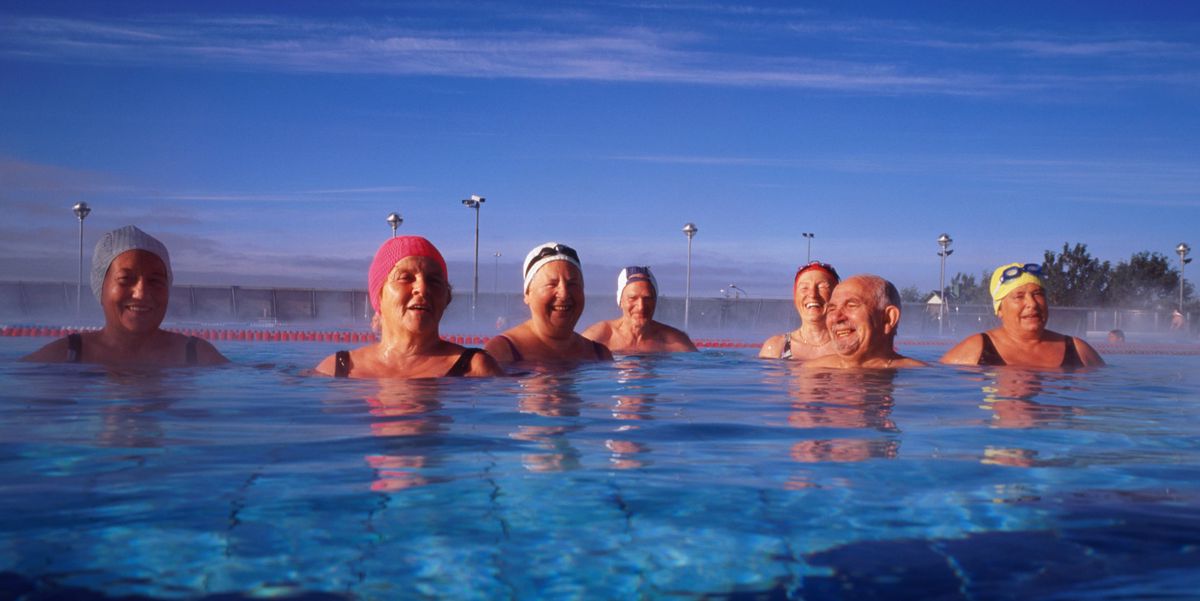 Groupe de personnes âgées nageant dans une piscine extérieure en Islande sous un ciel bleu clair.