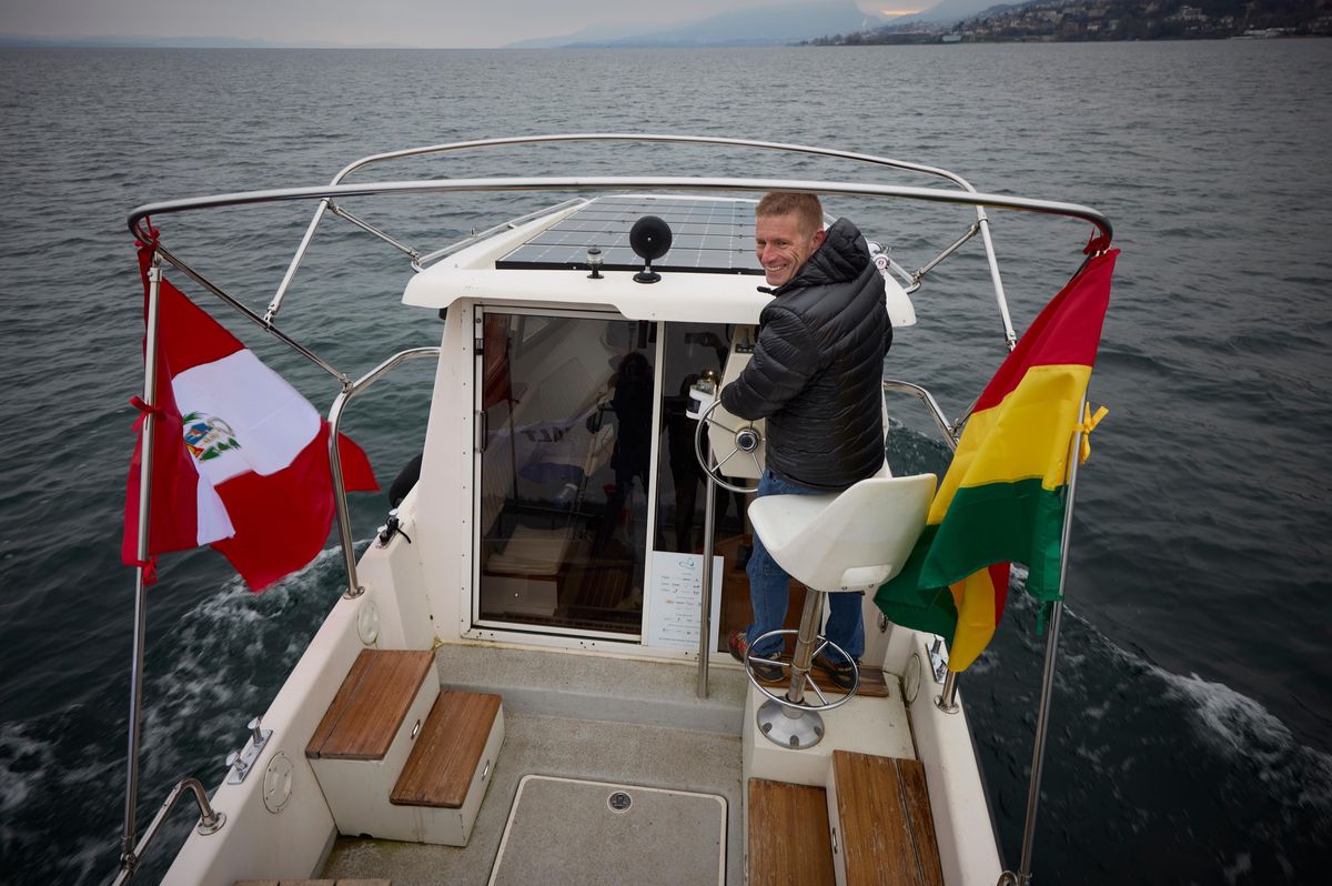 Raphael Domjan à la barre du Planet Solar 2 sur le lac de Neuchâtel, avec des drapeaux bolivien et péruvien à l’arrière du bateau.