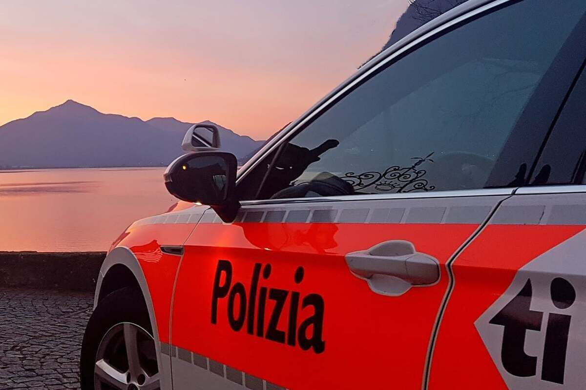 Polizeifahrzeug mit Aufschrift «Polizia» vor einem See mit Bergen und Abendhimmel im Kanton Tessin.