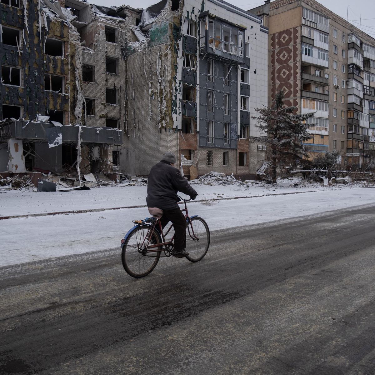 Ein Mann fährt Fahrrad in einer verschneiten Strasse in Pokrowsk, Ukraine, im Dezember 2024. Im Hintergrund sind beschädigte Gebäude zu sehen.